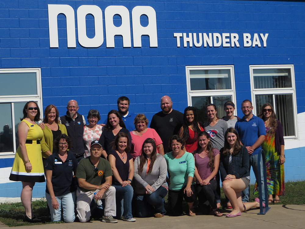 people posing for a group picture infront of the thunder bay national marine sancutary office